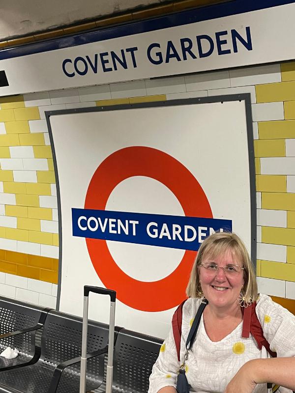 Lady sitting in front of a Covent Garden Tube sign.