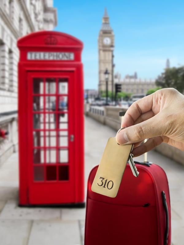 Hand holding a hotel key with Big Ben and a red telephone box in the background.