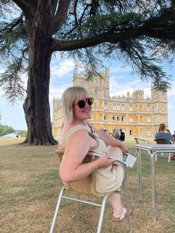 Highclere Castle with a lady sitting in a chair in front of it.