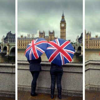 Two people in London in November holding Union Jack umbrellas with Big Ben and the Houses of Parliament in the background.