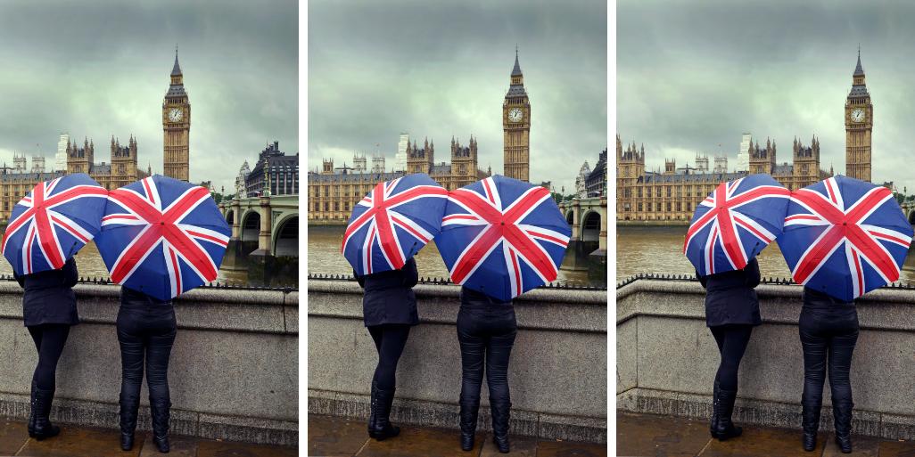 Two people in London in November holding Union Jack umbrellas with Big Ben and the Houses of Parliament in the background.