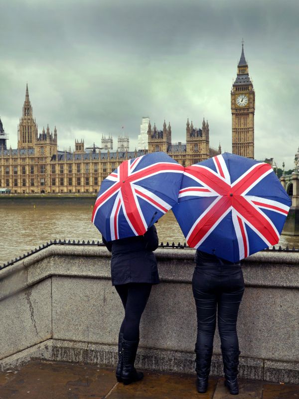 Two people holding Union Jack umbrellas in front of Big Ben and the Houses of Parliament in London.