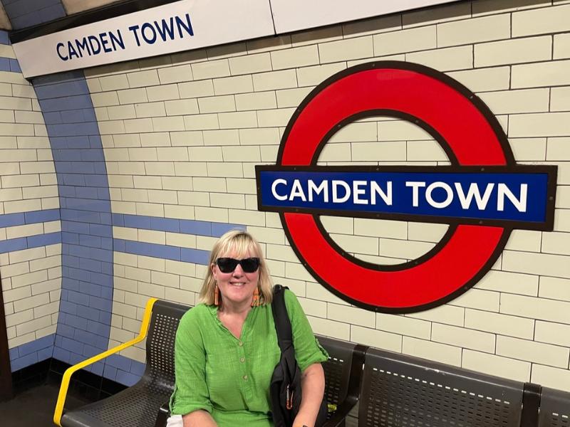 Lady sitting next to a Camden Town tube sign.