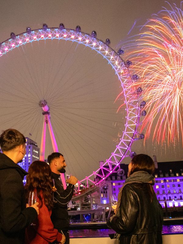 Passengers with champagne on the deck of a City Cruises boat watching the New Year's Eve fireworks over the London Eye and County Hall.
