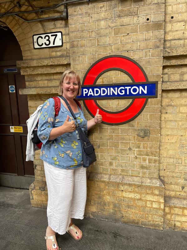 Things to do in Paddington include taking a photo next to the tube sign like the lady in this image.