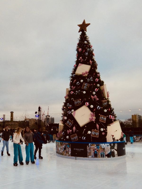 Skaters on the Glide ice rink at Battersea Power Station around a Christmas tree.