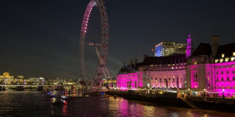 The London Eye and County Hall lit up in pink at night, seen from Westminster Bridge.