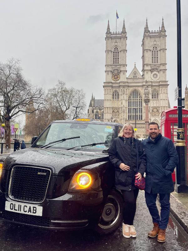 A man and a lady standing next to a london cab.