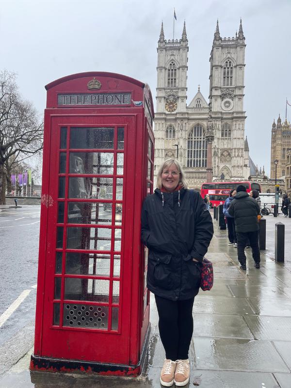 A lady standing in front of Westminster Abbey and next to a red phone box.