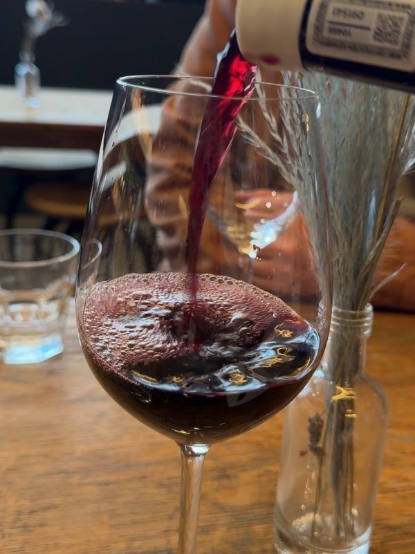Red wine being poured into a glass on a wooden table at a wine bar
