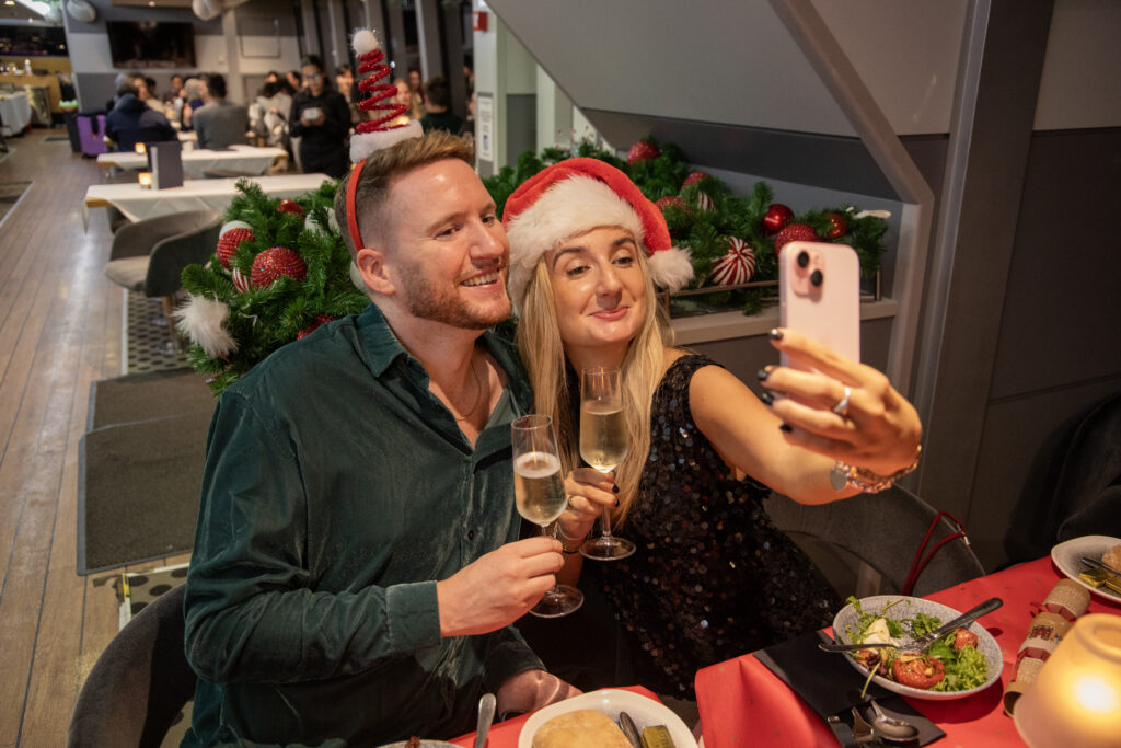 A couple with glasses of champagne on the deck of a City Cruises Christmas cruise on the Thames