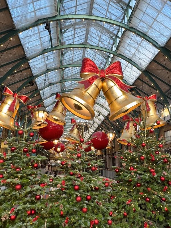 Giant gold bells and red baubles hanging above Christmas trees in Covent Garden market.