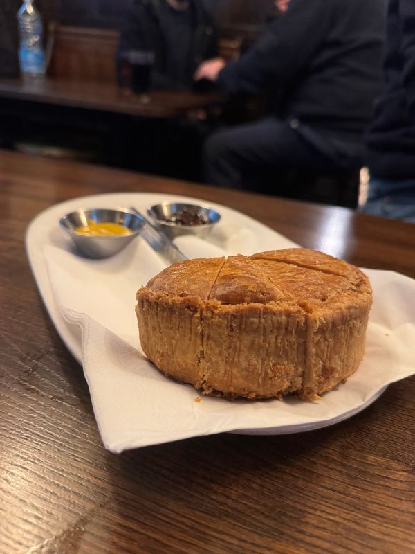 A whole hand-raised pork pie with mustard and chutney on a historic pub table