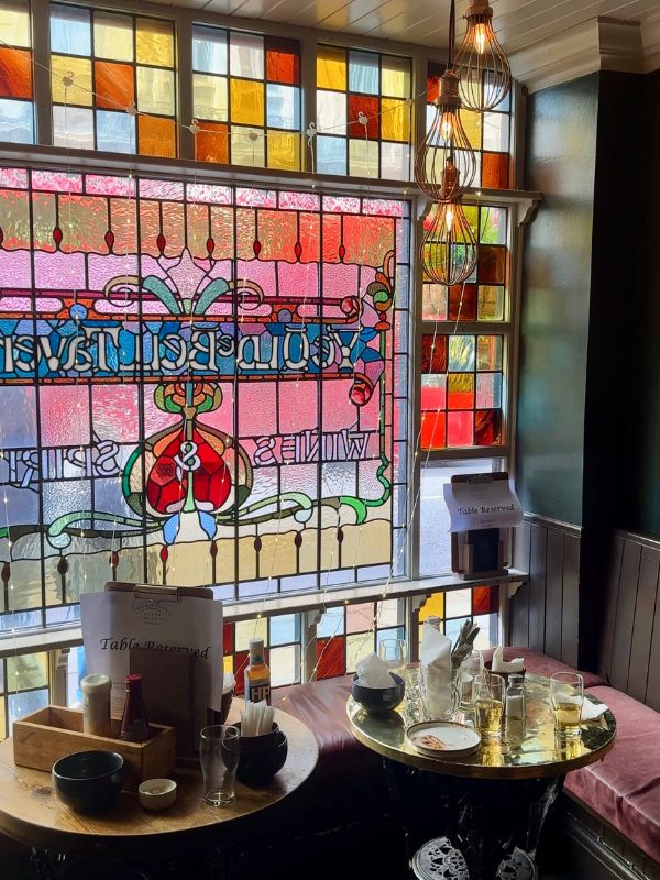 Victorian stained glass windows and a reserved brass table inside a historic London pub