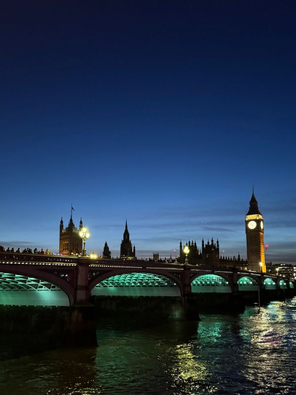 The Houses of Parliament and Big Ben at dusk with Westminster Bridge lit green.