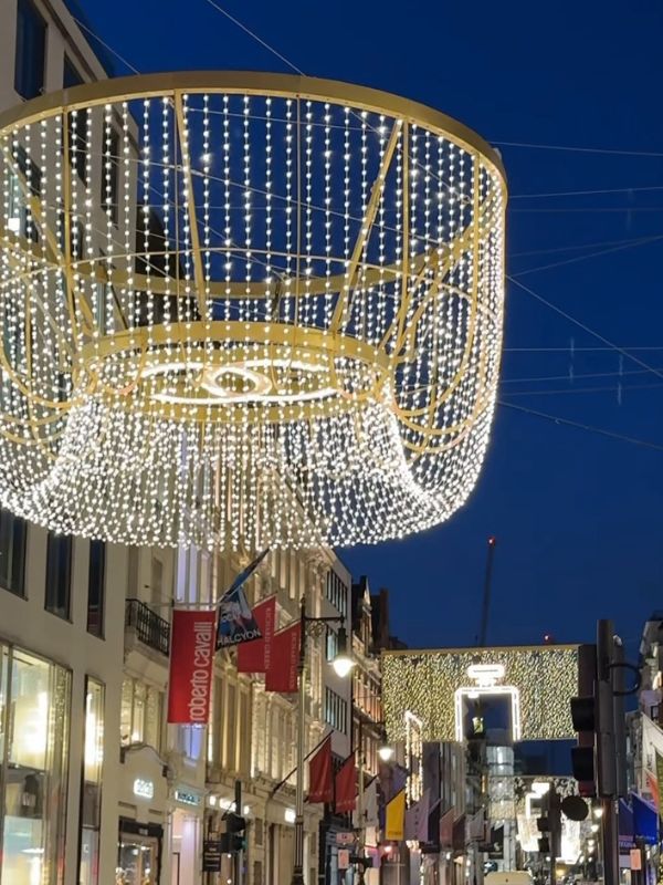 Gold chandelier Christmas lights hanging above New Bond Street at dusk.