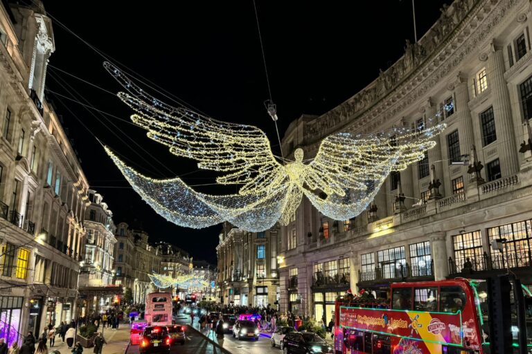 The Spirit of Christmas angel lights above Regent Street at night, with buses and taxis passing beneath.