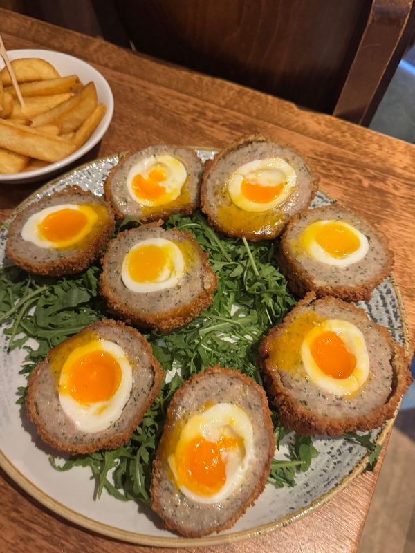 A plate of halved scotch eggs with soft orange yolks and rocket