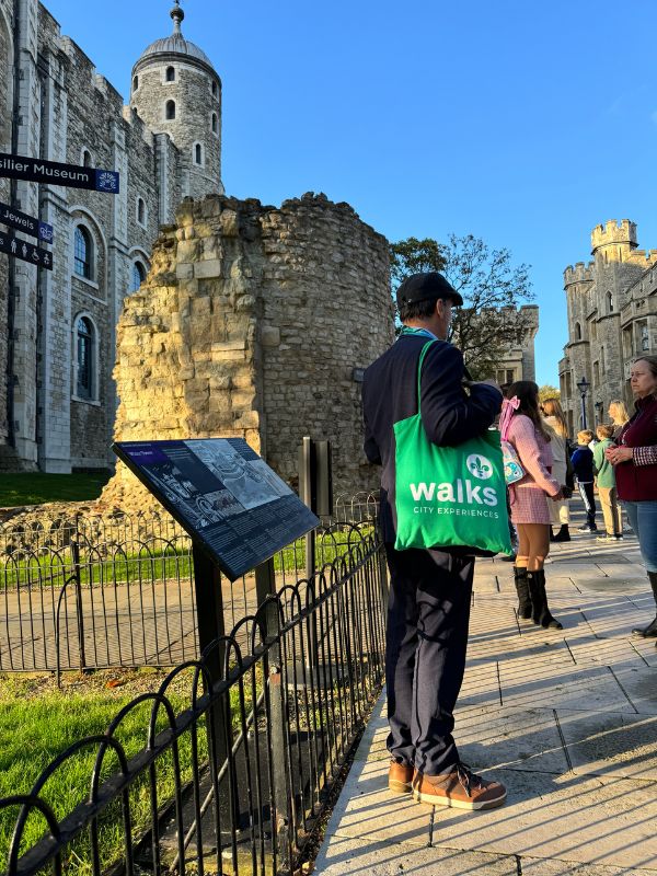 A tour guide with a green Walks bag beside the White Tower at the Tower of London