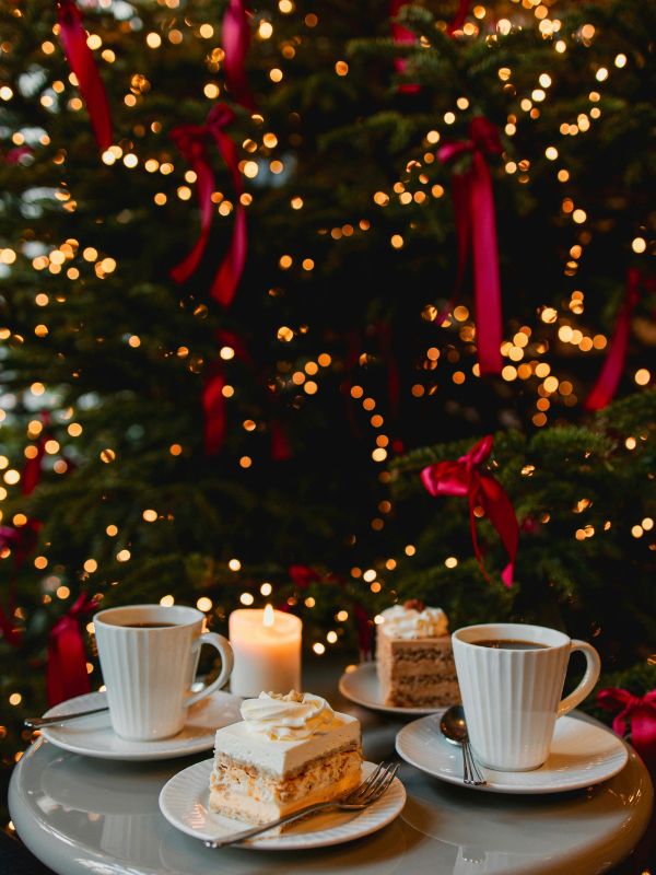 Cake and hot drinks on a table beside a Christmas tree, the setting most London hotels aim for with their festive afternoon tea