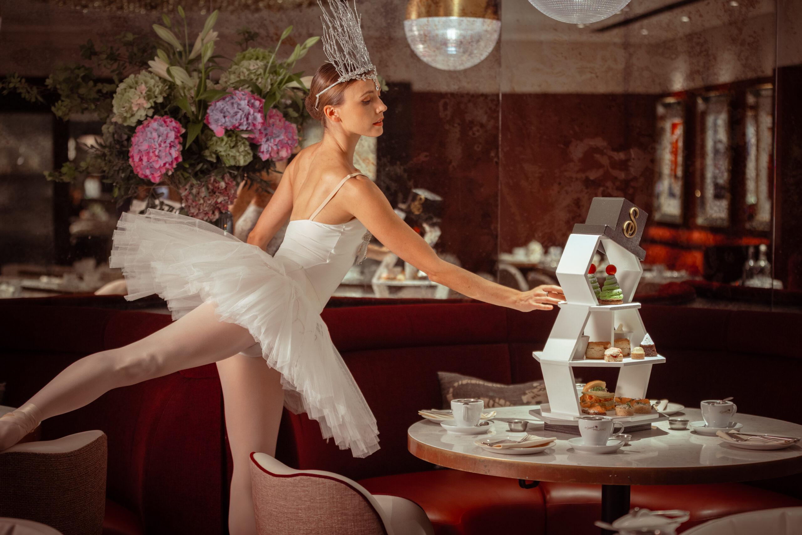 A Snow Ballerina reaching for a cake from the snowman afternoon tea stand at Strand Palace’s Frosted Cocoa Christmas afternoon tea