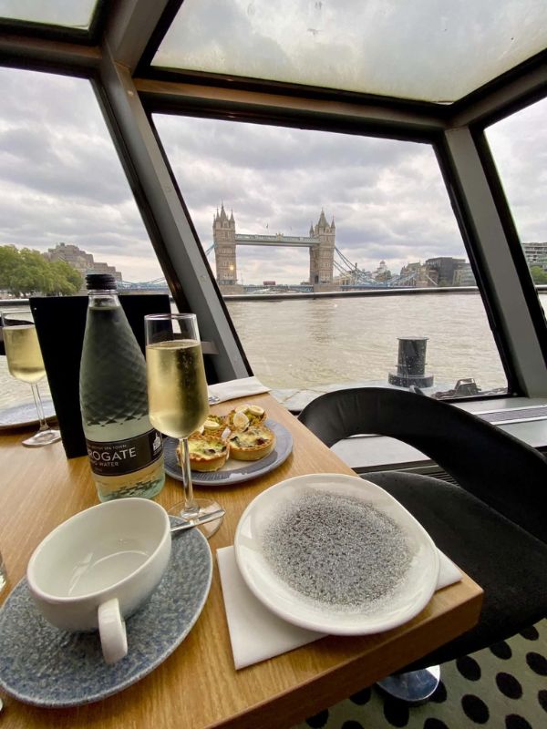 Afternoon tea cruise table with prosecco and a view of Tower Bridge through the window of a City Cruises boat