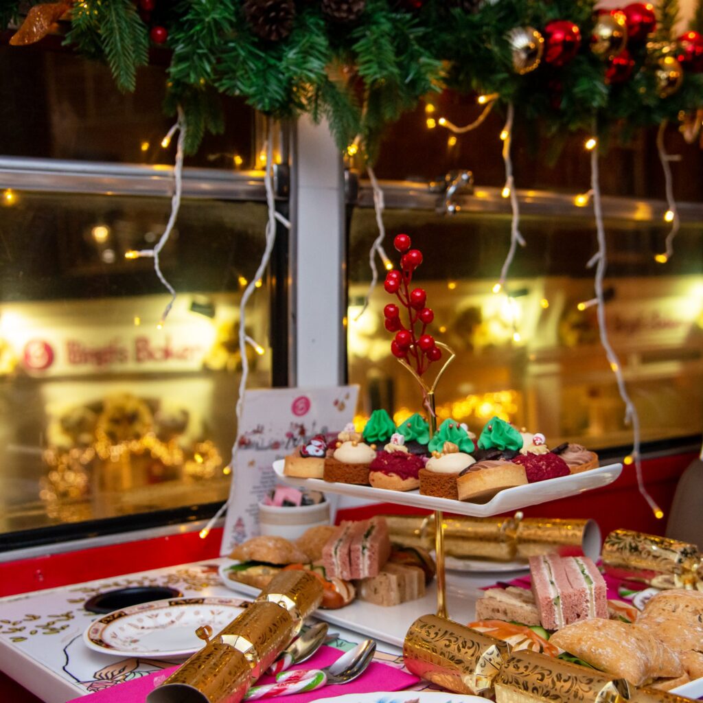 Christmas afternoon tea on board the Brigit’s Bakery bus, with festive cakes, finger sandwiches and gold crackers on a table by a window strung with fairy lights