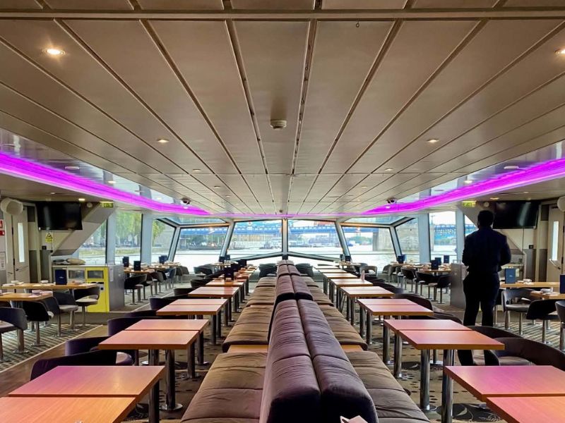Interior saloon of a City Cruises boat with rows of tables, bench seating and large panoramic windows