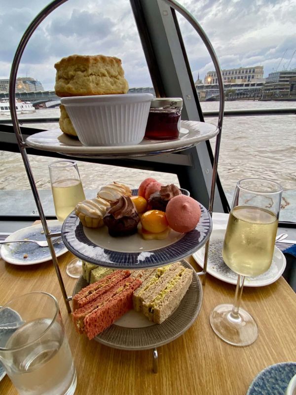 Three-tier afternoon tea stand with scones, pastries and finger sandwiches beside a glass of prosecco on a City Cruises boat